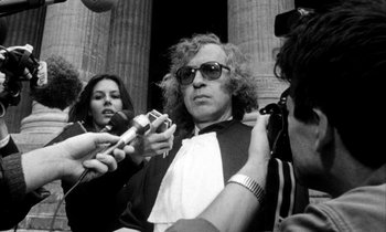 Movie still from “Man Bites Dog” (1992), directed by Benoît Poelvoorde – A man is being interviewed by a group of reporters; Medium shot, Over the shoulder angle