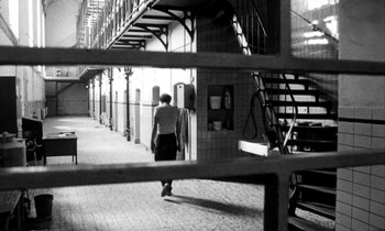 Movie still from “Man Bites Dog” (1992), directed by Benoît Poelvoorde – A man walking down a hallway in a building; Wide shot, High angle