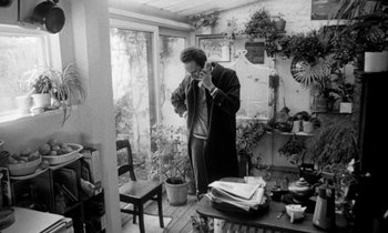 Movie still from “Man Bites Dog” (1992), directed by Benoît Poelvoorde – A black and white photo of a man standing in a room with plants; Medium shot, High angle