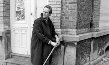 Movie still from “Man Bites Dog” (1992), directed by Benoît Poelvoorde – A black and white photo of a man holding a broom; Medium shot, Low angle