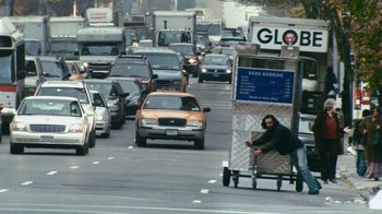 Movie still from “Man Push Cart” (2005), directed by Ramin Bahrani – A person riding a bike on a cart on a busy street; Wide shot, Low angle