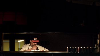 Movie still from “Man Push Cart” (2005), directed by Ramin Bahrani – A man sitting at a table in front of a drink; Medium shot, Low angle