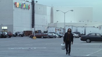 Movie still from “Man Push Cart” (2005), directed by Ramin Bahrani – A man walking down the street holding a bag of food; Wide shot, Low angle