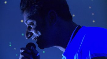 Movie still from “Man Push Cart” (2005), directed by Ramin Bahrani – A person singing into a microphone; Extreme Close Up shot, Low angle