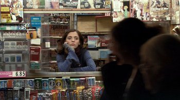 Movie still from “Man Push Cart” (2005), directed by Ramin Bahrani – A woman sitting in front of a counter in a store; Medium shot, Over the shoulder angle