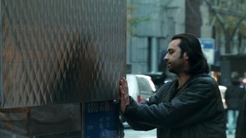 Movie still from “Man Push Cart” (2005), directed by Ramin Bahrani – A man standing next to a metal fence; Medium shot, Low angle