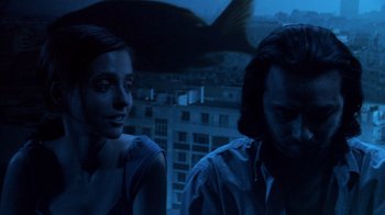 Movie still from “Man Push Cart” (2005), directed by Ramin Bahrani – A man and a woman sitting next to each other in front of a building; Medium shot, High angle