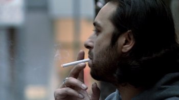 Movie still from “Man Push Cart” (2005), directed by Ramin Bahrani – A person holding a cigarette in his mouth; Close Up shot, Low angle