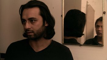 Movie still from “Man Push Cart” (2005), directed by Ramin Bahrani – A man with long black hair looking at himself in a mirror; Close Up shot, Low angle