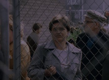 Movie still from “Man of Iron” (1981), directed by Andrzej Wajda – An older woman standing in front of a chain link fence; Medium shot, Over the shoulder angle