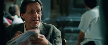 Movie still from “Man on Fire” (2004), directed by Tony Scott – An older man sitting in a chair holding a cell phone; Close Up shot, Over the shoulder angle