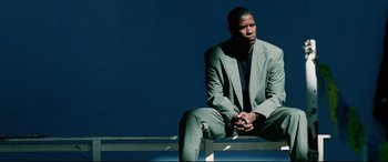 Movie still from “Man on Fire” (2004), directed by Tony Scott – A man in a suit sitting on top of a bench; Medium shot, Low angle
