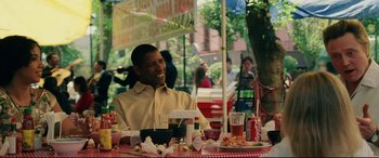 Movie still from “Man on Fire” (2004), directed by Tony Scott – A man sitting at an outdoor table with food on it; Medium shot, Over the shoulder angle