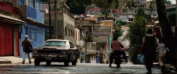 Movie still from “Man on Fire” (2004), directed by Tony Scott – A man riding a motorcycle down the middle of a street; Wide shot, High angle
