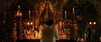Movie still from “Man on Fire” (2004), directed by Tony Scott – A woman standing in front of candles in front of an image of mary; Medium shot, Low angle