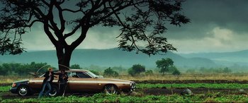 Movie still from “Man on Fire” (2004), directed by Tony Scott – An old car parked in the grass under a tree; Wide shot, Low angle