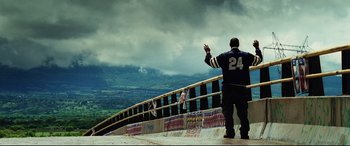 Movie still from “Man on Fire” (2004), directed by Tony Scott – A man standing on the side of a bridge waving; Wide shot, Low angle