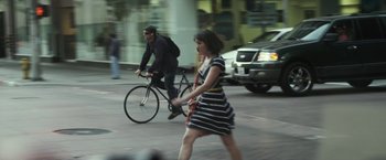 Movie still from “Maniac” (2012), directed by Franck Khalfoun – A woman walking across the street while a man on a bike rides by; Wide shot, High angle