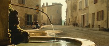 Movie still from “Manon of the Spring” (1986), directed by Claude Berri – People sitting on the side of the street and a fountain; Extreme Wide shot, Low angle