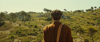 Movie still from “Manon of the Spring” (1986), directed by Claude Berri – A man standing on top of a hill looking out at a forest; Wide shot, Over the shoulder angle