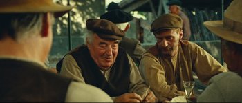 Movie still from “Manon of the Spring” (1986), directed by Claude Berri – A group of men sitting next to each other on a table; Medium shot, Over the shoulder angle