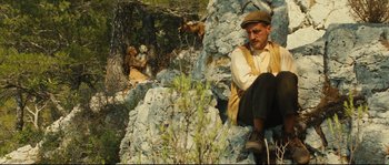 Movie still from “Manon of the Spring” (1986), directed by Claude Berri – A man sitting on top of a pile of rocks next to a tree; Wide shot, Low angle