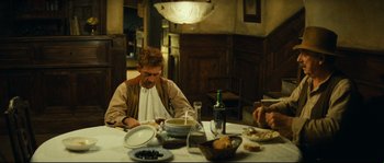 Movie still from “Manon of the Spring” (1986), directed by Claude Berri – A man sitting at a table with a bowl of food; Medium shot, High angle