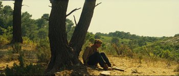 Movie still from “Manon of the Spring” (1986), directed by Claude Berri – A man sitting on the ground next to a tree; Wide shot, Low angle