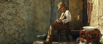 Movie still from “Manon of the Spring” (1986), directed by Claude Berri – A man sitting on top of a wooden chair in a room; Wide shot, Low angle