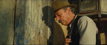 Movie still from “Manon of the Spring” (1986), directed by Claude Berri – An older man in a hat and a tie holding a cell phone; Close Up shot, Low angle