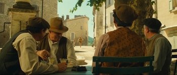 Movie still from “Manon of the Spring” (1986), directed by Claude Berri – Two men sitting at a table in front of a building; Wide shot, Over the shoulder angle