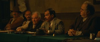 Movie still from “Manon of the Spring” (1986), directed by Claude Berri – A group of men sitting at a table; Medium shot, High angle