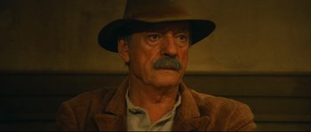 Movie still from “Manon of the Spring” (1986), directed by Claude Berri – An older man wearing a brown hat and a brown jacket; Close Up shot, Low angle