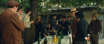 Movie still from “Manon of the Spring” (1986), directed by Claude Berri – A group of people standing around a table with wine bottles; Wide shot, High angle