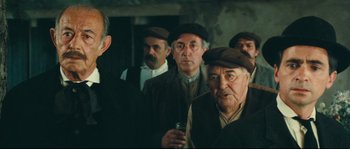 Movie still from “Manon of the Spring” (1986), directed by Claude Berri – A group of men standing next to each other in a room; Medium shot, Low angle