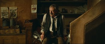 Movie still from “Manon of the Spring” (1986), directed by Claude Berri – An older man sitting in a chair in a room; Medium shot, Low angle