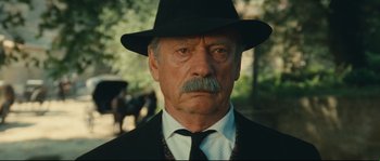 Movie still from “Manon of the Spring” (1986), directed by Claude Berri – An older man wearing a black hat and a black tie; Close Up shot, Low angle