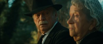 Movie still from “Manon of the Spring” (1986), directed by Claude Berri – An older man wearing a black hat and a black tie; Close Up shot, Over the shoulder angle