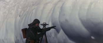 Movie still from “Map of the Human Heart” (1992), directed by Vincent Ward – A man is looking through a telescope in front of a wall of water; Medium shot, High angle