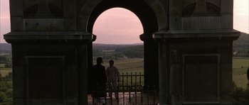 Movie still from “Map of the Human Heart” (1992), directed by Vincent Ward – Two people are standing in front of an arched doorway; Extreme Wide shot, Over the shoulder angle