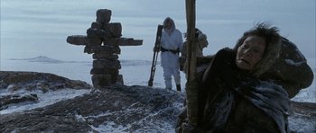 Movie still from “Map of the Human Heart” (1992), directed by Vincent Ward – A man in a snow suit standing next to a pile of rocks; Wide shot, Over the shoulder angle