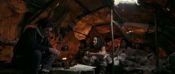 Movie still from “Map of the Human Heart” (1992), directed by Vincent Ward – A group of people sitting around a table in a hut; Medium shot, High angle