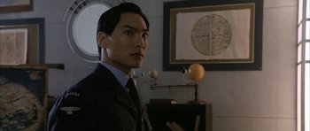 Movie still from “Map of the Human Heart” (1992), directed by Vincent Ward – A man wearing a suit and tie standing in a room; Close Up shot, Over the shoulder angle