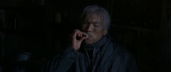 Movie still from “Map of the Human Heart” (1992), directed by Vincent Ward – An older man smoking a cigarette in the dark; Medium shot, High angle