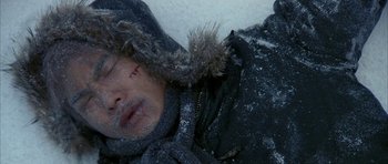 Movie still from “Map of the Human Heart” (1992), directed by Vincent Ward – A man in a black jacket is laying in the snow; Close Up shot, High angle
