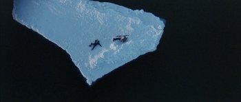 Movie still from “Map of the Human Heart” (1992), directed by Vincent Ward – Two skiers are laying on the snow near a rock; Extreme Wide shot, Overhead angle