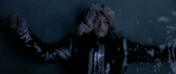 Movie still from “Map of the Human Heart” (1992), directed by Vincent Ward – A man in a black jacket and a fur hat is laying down; Medium shot, Overhead angle