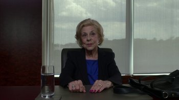 Movie still from “Maps to the Stars” (2014), directed by David Cronenberg – An older woman sitting at a table in front of a glass of water; Medium shot, Over the shoulder angle