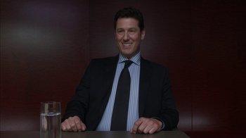 Movie still from “Maps to the Stars” (2014), directed by David Cronenberg – A man sitting at a table in a suit and tie; Medium shot, Low angle