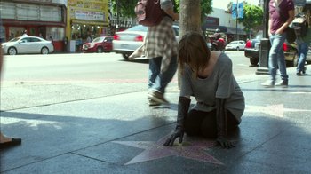 Movie still from “Maps to the Stars” (2014), directed by David Cronenberg – A woman sitting on the ground with her hand on a star on the sidewalk; Wide shot, High angle